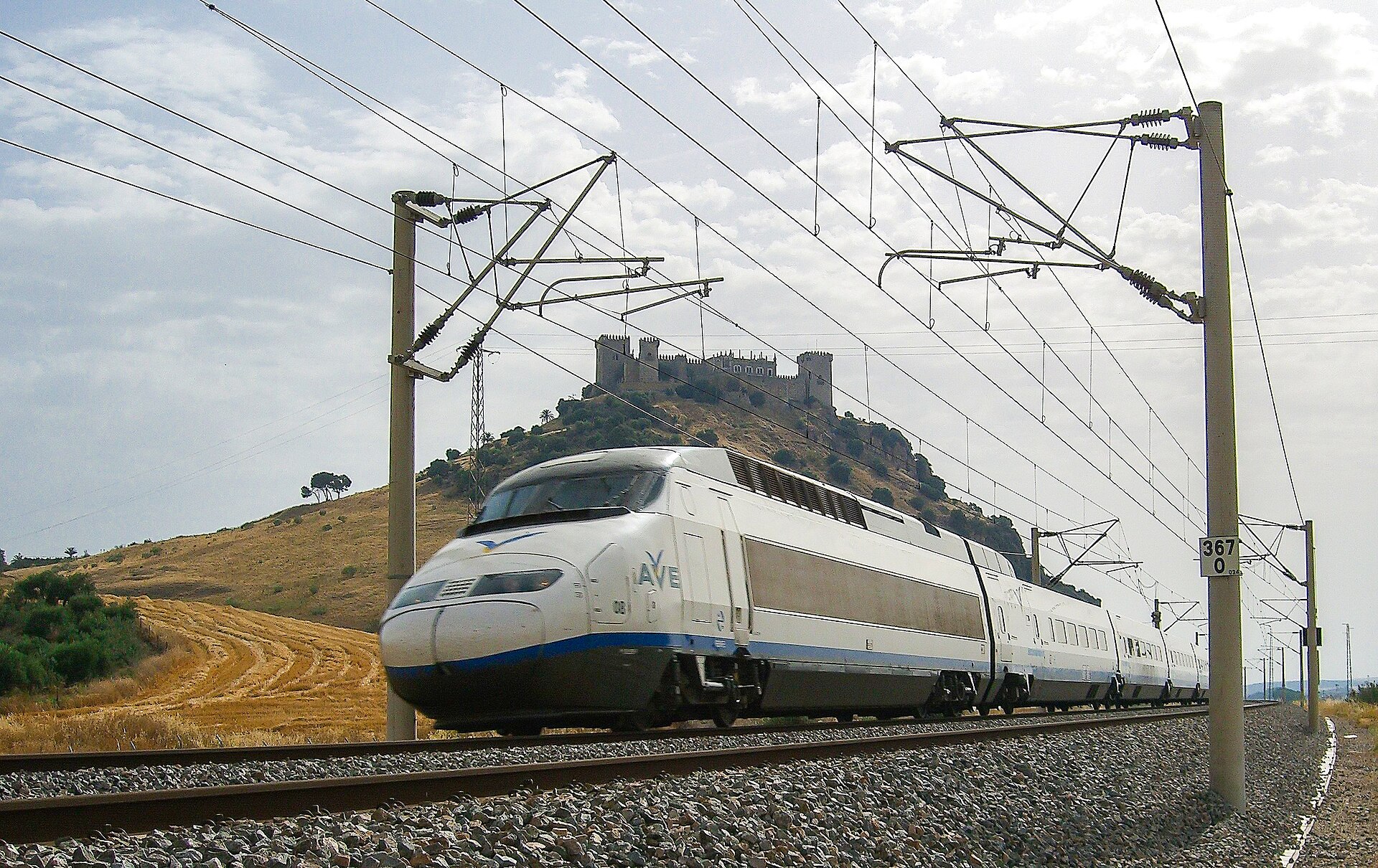 Un tren de alta velocidad AVE de Renfe pasando junto a un castillo en lo alto de una colina en el campo español